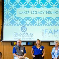 Three alumni sit in front of a crowded room of people